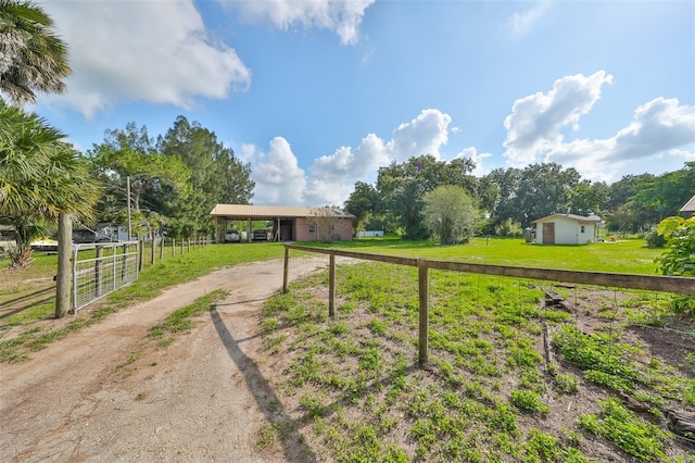 view of yard featuring dirt driveway, a carport, a rural view, and fence