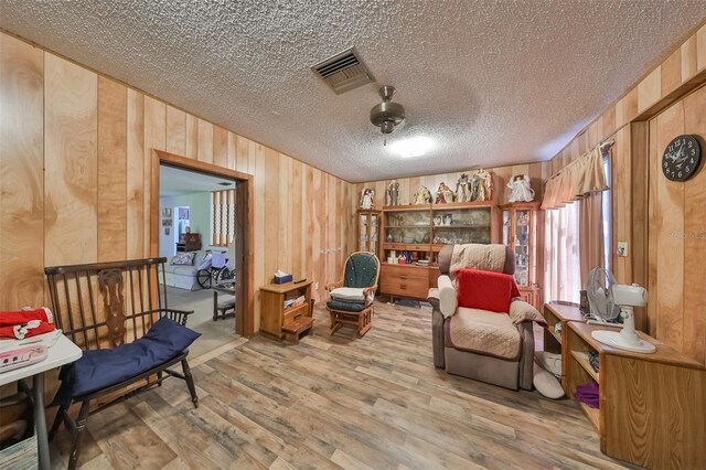 living area featuring a textured ceiling, wooden walls, visible vents, and wood finished floors