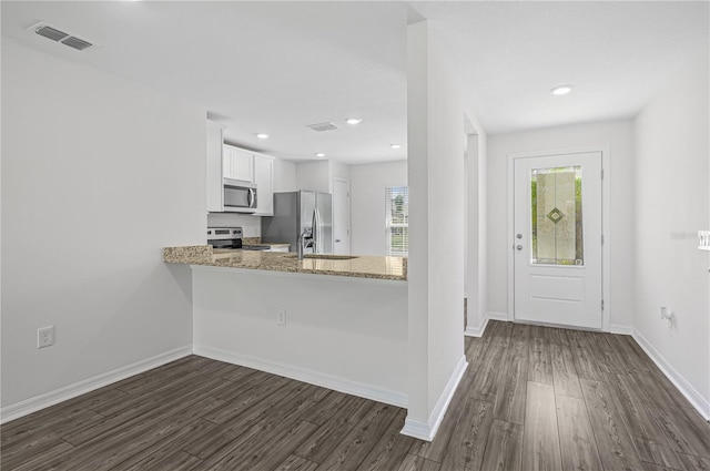 kitchen with kitchen peninsula, white cabinetry, stainless steel appliances, dark wood-type flooring, and light stone counters