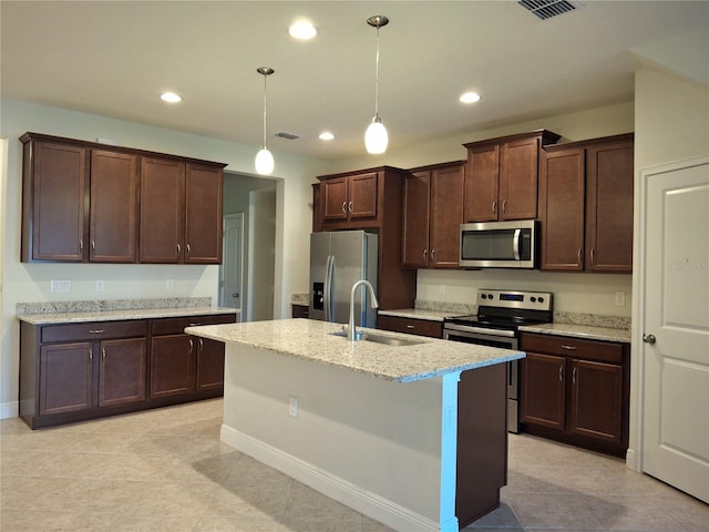 kitchen featuring an island with sink, sink, light stone countertops, pendant lighting, and appliances with stainless steel finishes