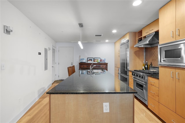 kitchen featuring high end appliances, dark stone counters, sink, an island with sink, and light hardwood / wood-style floors