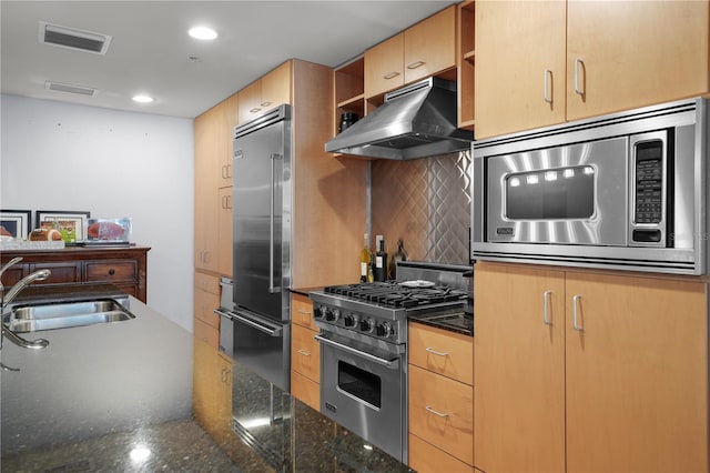 kitchen with light brown cabinets, backsplash, dark stone counters, sink, and premium appliances