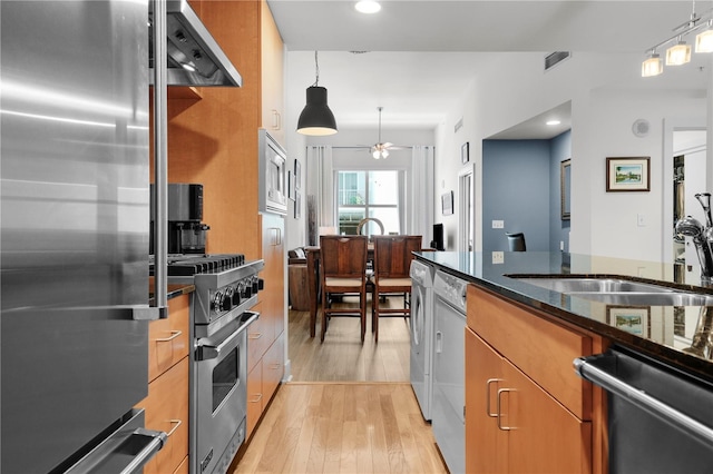 kitchen with sink, light hardwood / wood-style flooring, dark stone countertops, appliances with stainless steel finishes, and decorative light fixtures