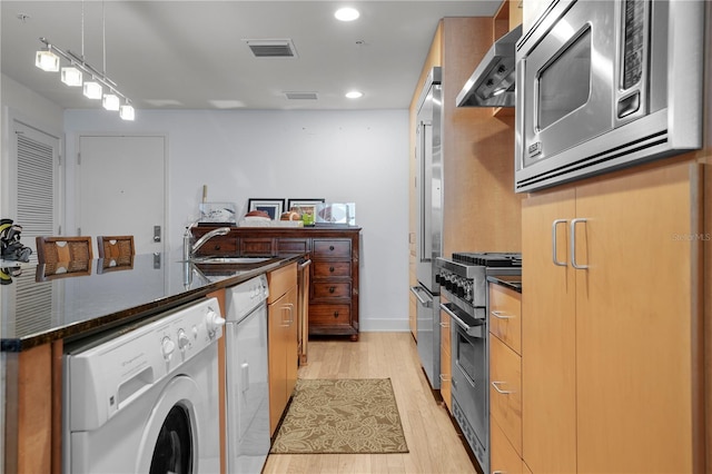 kitchen featuring sink, wall chimney exhaust hood, appliances with stainless steel finishes, light hardwood / wood-style floors, and washer / dryer