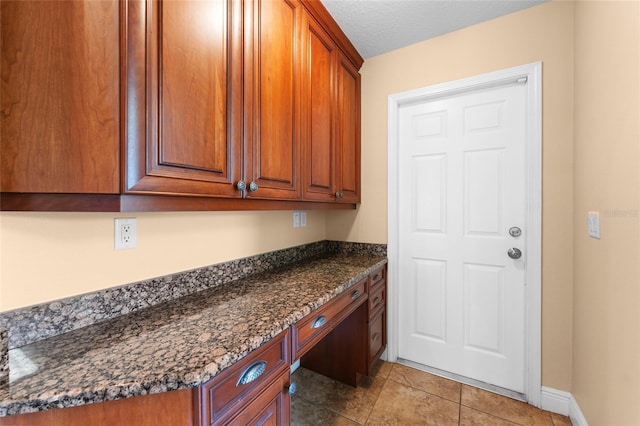 kitchen with light tile patterned floors, dark stone countertops, built in desk, and a textured ceiling