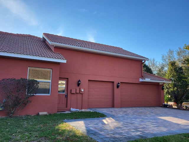 exterior space with a garage, a tiled roof, decorative driveway, and stucco siding