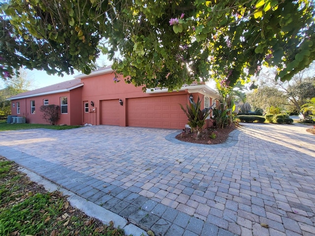 view of front of house featuring a garage, central AC unit, decorative driveway, and stucco siding