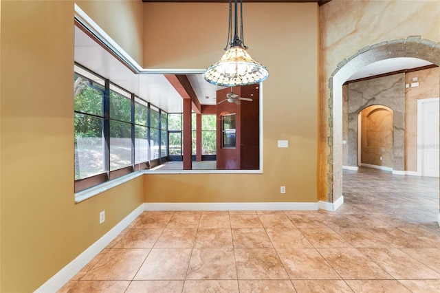 unfurnished room featuring arched walkways, ceiling fan, light tile patterned floors, and baseboards