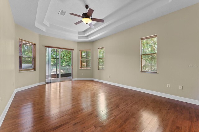 spare room with a tray ceiling, a healthy amount of sunlight, visible vents, and dark wood finished floors