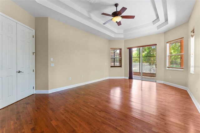 unfurnished room with ceiling fan, a tray ceiling, wood finished floors, and baseboards