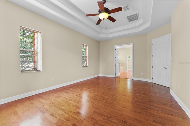 unfurnished room with wood finished floors, a raised ceiling, visible vents, and baseboards