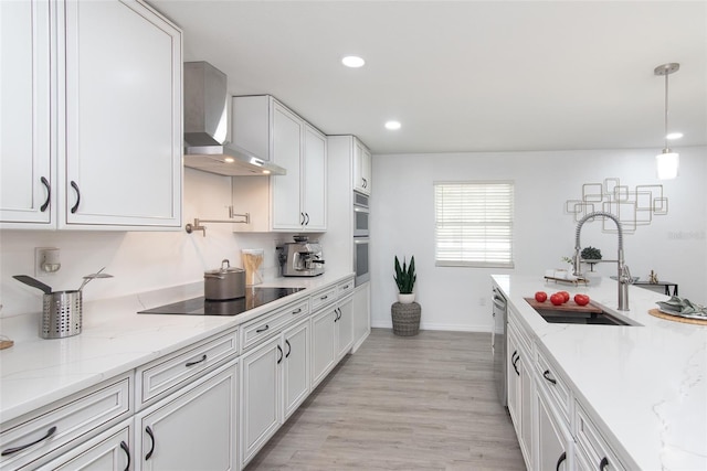 kitchen with light wood-type flooring, sink, wall chimney range hood, decorative light fixtures, and white cabinets