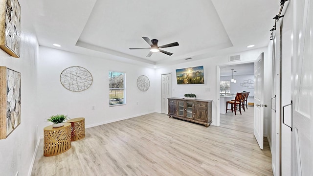 living room featuring light wood-type flooring, a raised ceiling, and plenty of natural light