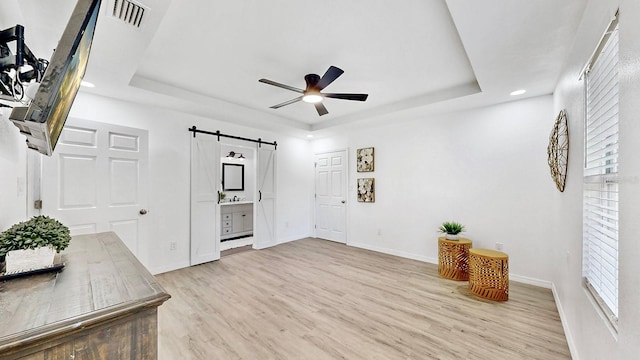 sitting room featuring ceiling fan, a barn door, a raised ceiling, and light hardwood / wood-style floors