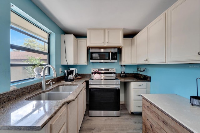 kitchen featuring stainless steel appliances, light stone counters, light wood-type flooring, and sink