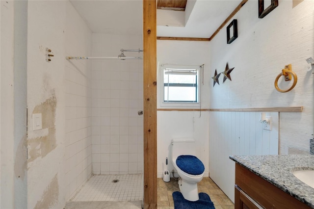 bathroom featuring tile flooring, a tile shower, ornamental molding, toilet, and vanity