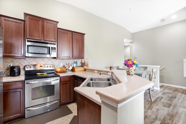 kitchen with sink, light hardwood / wood-style flooring, appliances with stainless steel finishes, kitchen peninsula, and backsplash