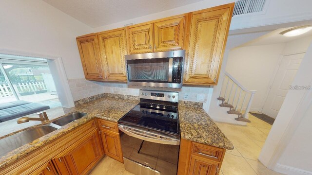 kitchen featuring vaulted ceiling, light tile flooring, dark stone countertops, backsplash, and appliances with stainless steel finishes