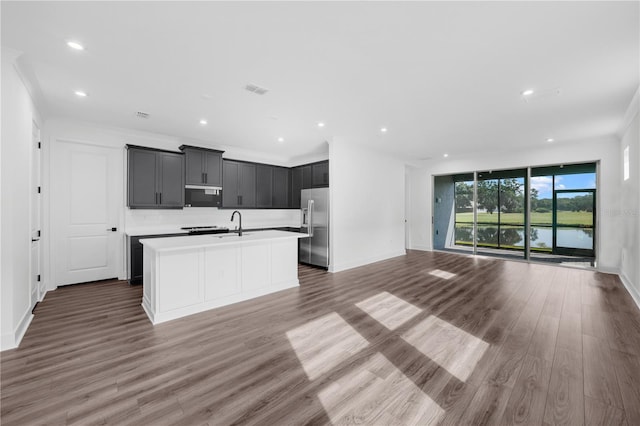 kitchen with crown molding, a center island with sink, dark wood-type flooring, and stainless steel refrigerator with ice dispenser