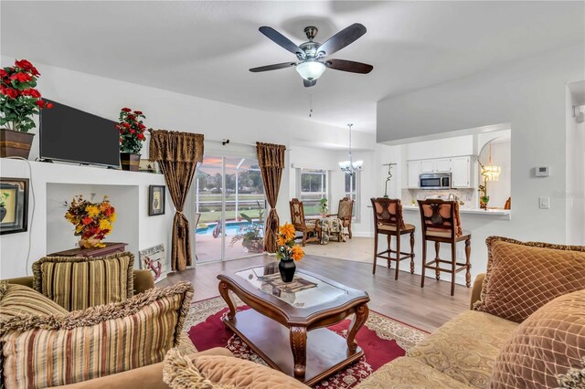 living room with light wood-type flooring and ceiling fan with notable chandelier