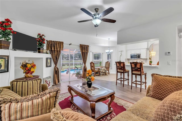 living area with ceiling fan with notable chandelier and light wood-type flooring