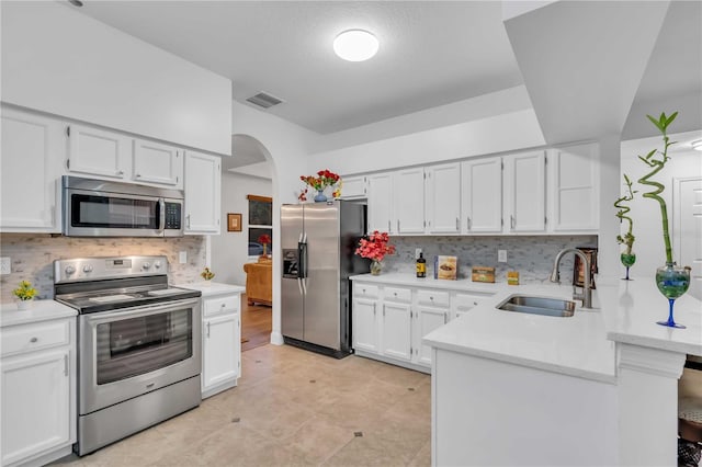 kitchen with visible vents, a sink, arched walkways, appliances with stainless steel finishes, and a peninsula