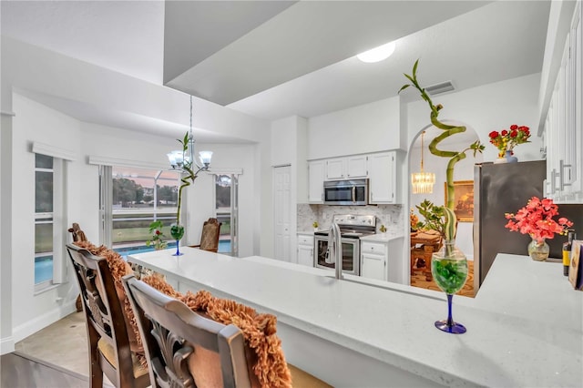 kitchen featuring decorative backsplash, white cabinetry, stainless steel appliances, and an inviting chandelier