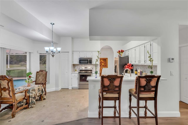 kitchen featuring appliances with stainless steel finishes, a peninsula, an inviting chandelier, light countertops, and decorative backsplash