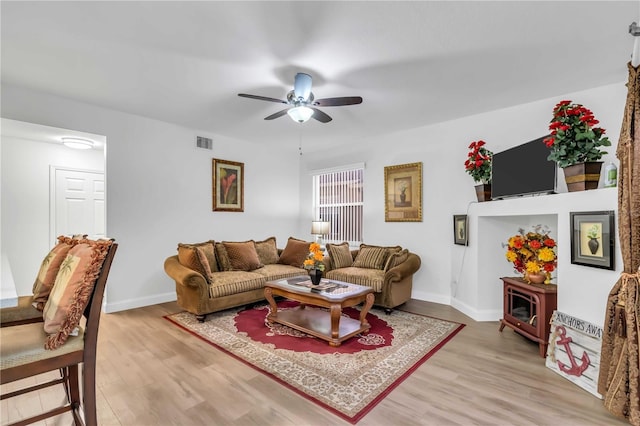 living room featuring light wood-type flooring, visible vents, baseboards, and a ceiling fan