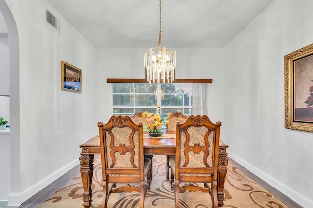 dining room featuring visible vents, wood finished floors, arched walkways, baseboards, and a chandelier