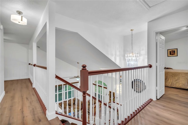 hall with an upstairs landing, lofted ceiling, wood finished floors, an inviting chandelier, and baseboards