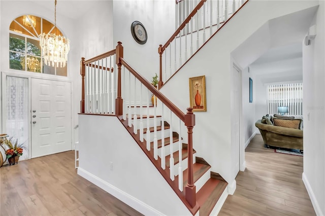 foyer with a wealth of natural light, a notable chandelier, a towering ceiling, and wood finished floors