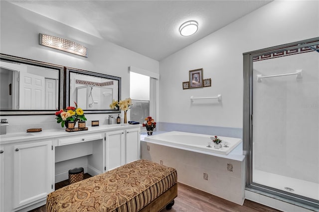 bathroom with wood finished floors, double vanity, a sink, a shower stall, and a bath