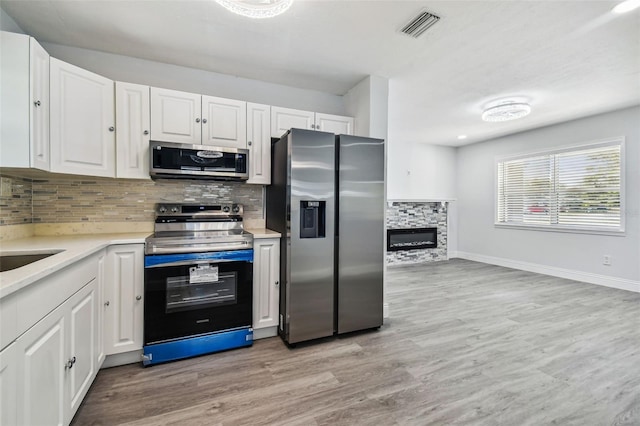 kitchen featuring white cabinetry, a fireplace, stainless steel appliances, and light wood-type flooring