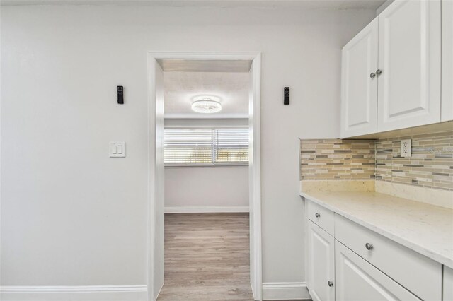 interior space with backsplash, light stone counters, white cabinets, and light wood-type flooring