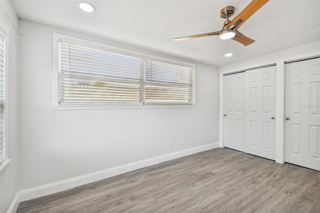 unfurnished bedroom featuring multiple closets, ceiling fan, multiple windows, and light wood-type flooring