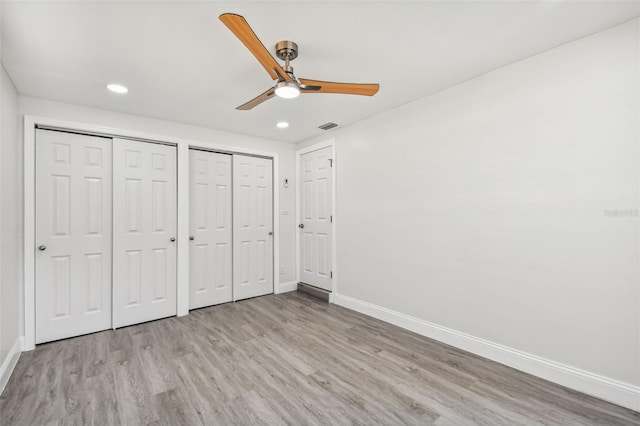 unfurnished bedroom featuring ceiling fan, light hardwood / wood-style flooring, and multiple closets