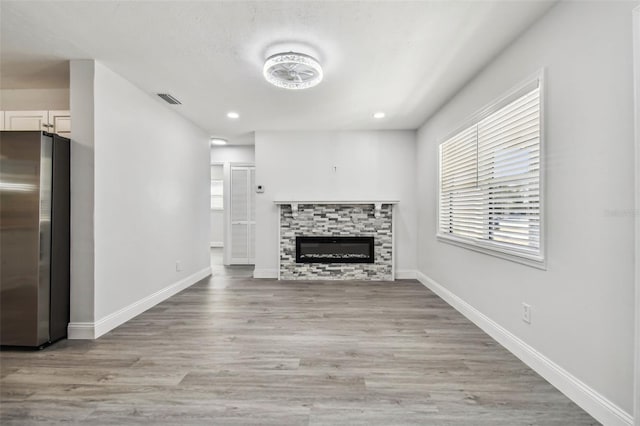 unfurnished living room featuring light hardwood / wood-style floors and a stone fireplace