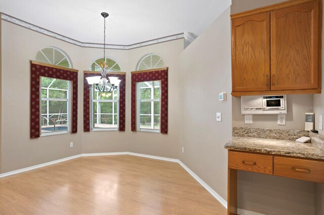 kitchen with an inviting chandelier, hanging light fixtures, light stone countertops, and light hardwood / wood-style floors