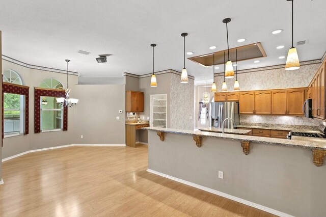 kitchen with backsplash, hanging light fixtures, light stone countertops, light wood-type flooring, and appliances with stainless steel finishes