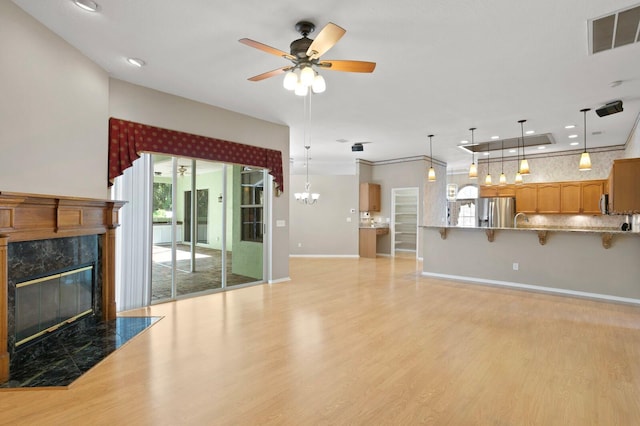 unfurnished living room with ceiling fan with notable chandelier, light hardwood / wood-style flooring, and a fireplace