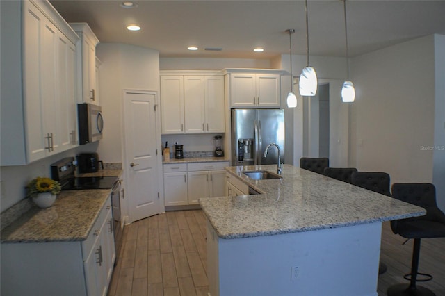 kitchen featuring sink, hanging light fixtures, an island with sink, stainless steel appliances, and white cabinets