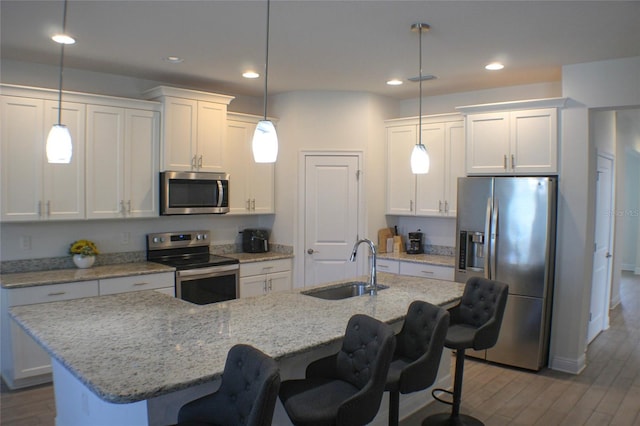 kitchen with white cabinetry, appliances with stainless steel finishes, a kitchen island with sink, and pendant lighting