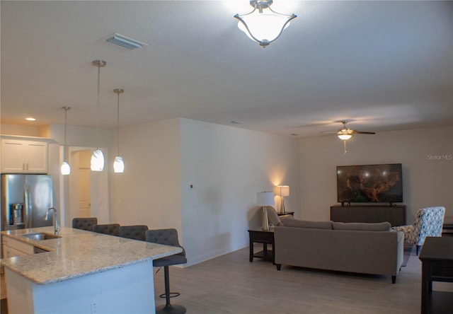 kitchen with light wood-type flooring, light stone countertops, a kitchen breakfast bar, white cabinetry, and ceiling fan