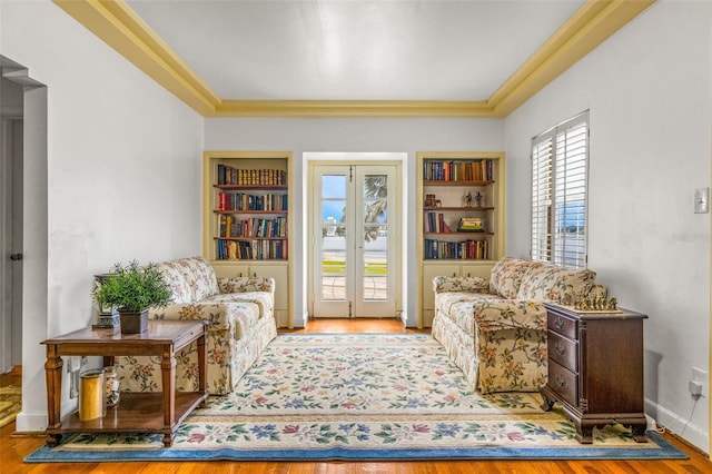 living area featuring wood-type flooring, built in shelves, french doors, and crown molding