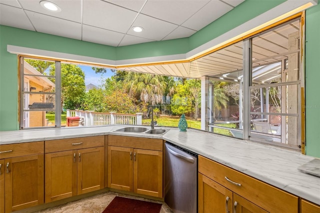 kitchen with dishwasher, brown cabinets, light countertops, a paneled ceiling, and a sink