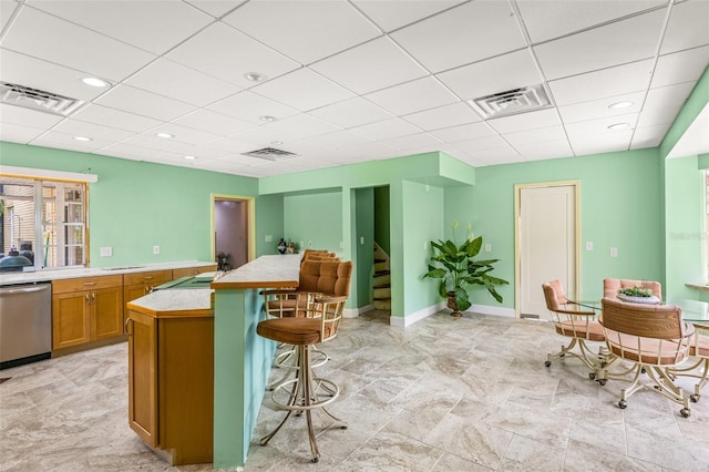 kitchen featuring light tile flooring, a breakfast bar area, dishwasher, and a drop ceiling