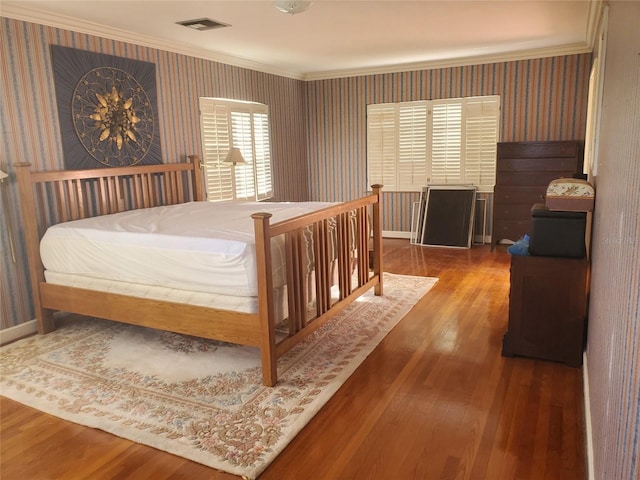 bedroom with crown molding, visible vents, wood finished floors, baseboards, and wallpapered walls