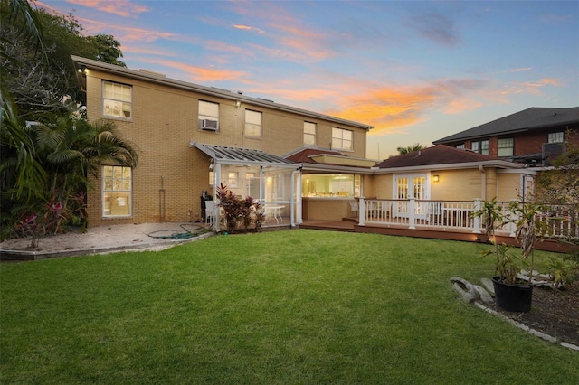 back of property at dusk featuring cooling unit, brick siding, a lawn, and a deck