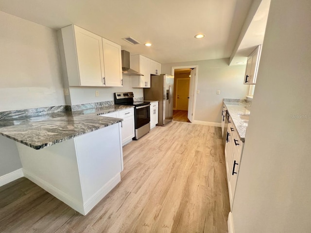 kitchen featuring light wood-type flooring, stainless steel appliances, wall chimney range hood, dark stone countertops, and white cabinets